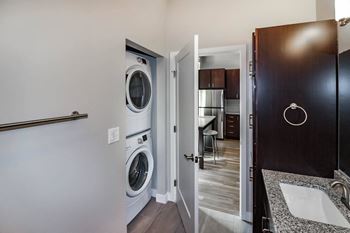 A laundry room with a washer and dryer, a bathroom with a sink and mirror, and a doorway leading to a kitchen. at RoCo Apartments, Fargo, ND 58102